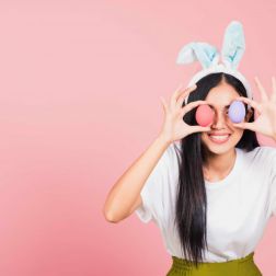 woman smiling wearing rabbit ears holding colorful Easter eggs front eyes