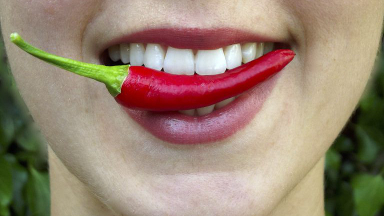Frau mit einer Chili zwischen den Zähnen