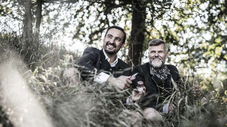 Zwei Jäger sitzen im Gras und essen eine Salami