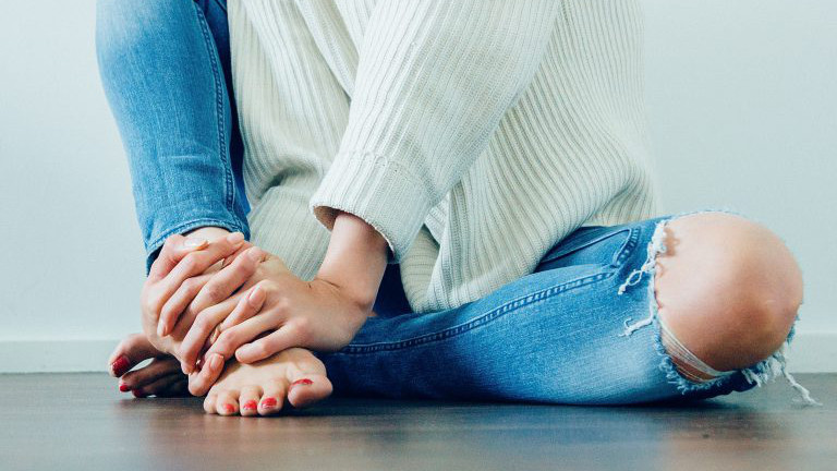 Frau in Jeans sitzt am Boden, barfuß