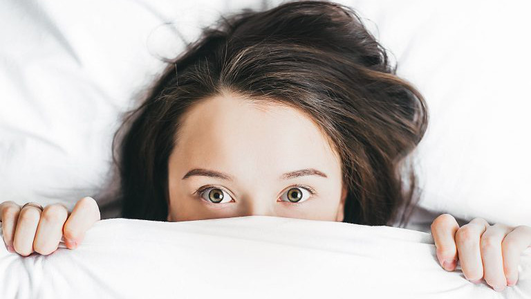 Frau zieht die Bettdecke über die Nase