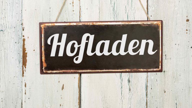 Altes Blechschild vor weißer Holzwand - Hofladen