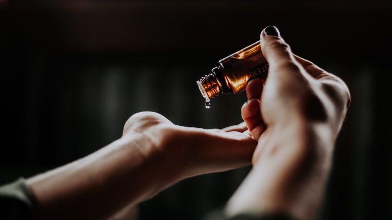 Öl tropft aus einer kleinen Flasche auf die Handfläche