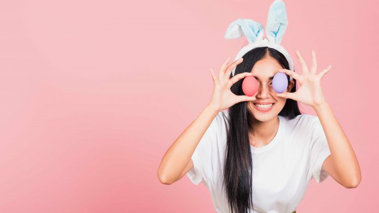 woman smiling wearing rabbit ears holding colorful Easter eggs front eyes