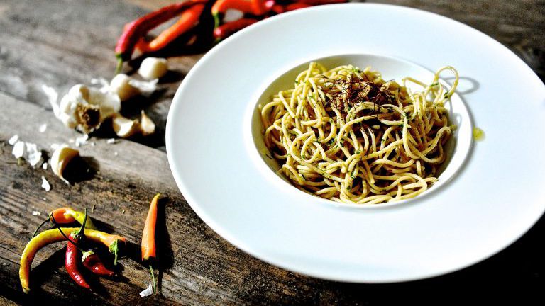 Teller mit Spaghetti, daneben Knoblauch und Chili