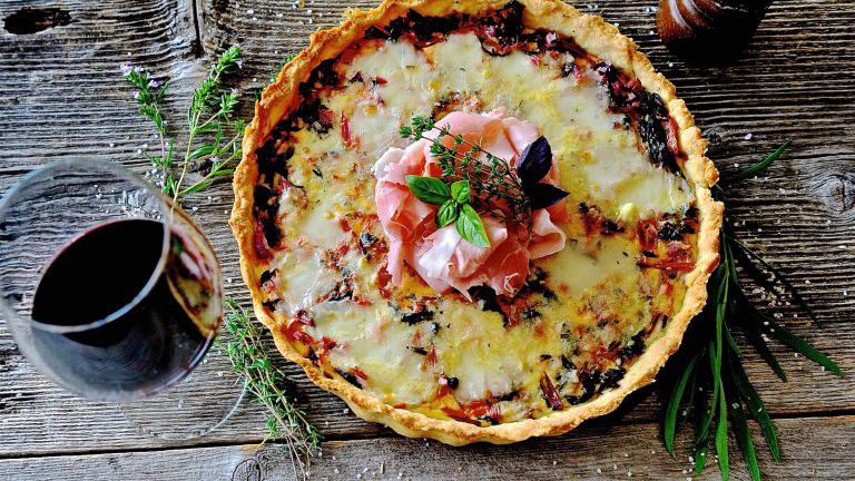 Quiche mit Schinken und einem Glas Rotwein auf Holzbrett